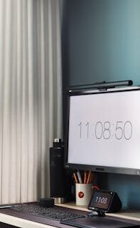 Minimalist home office setup with monitor and digital clock displaying time.